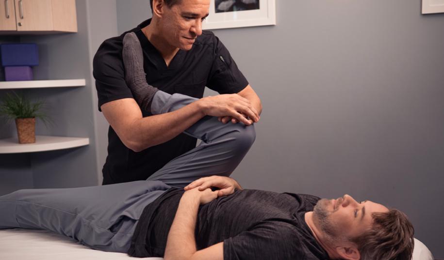 Man laying down on table as therapist stretches his leg. 