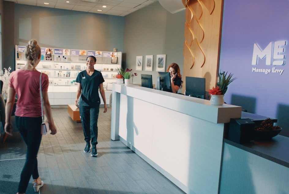 Women being greeted by massage therapist at Massage Envy clinic lobby. 