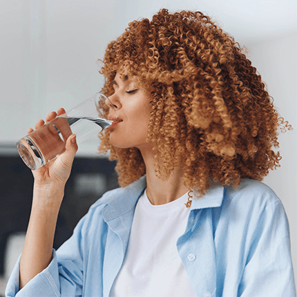 Woman with her eyes closed as she drinks a glass of water. 