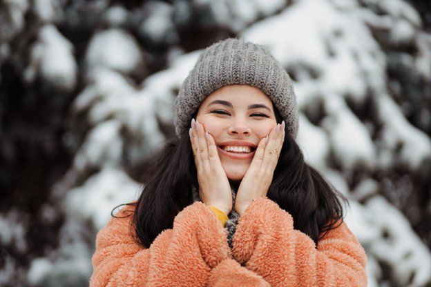 Woman outdoors in the snow smiling as she puts her hands to her face. 